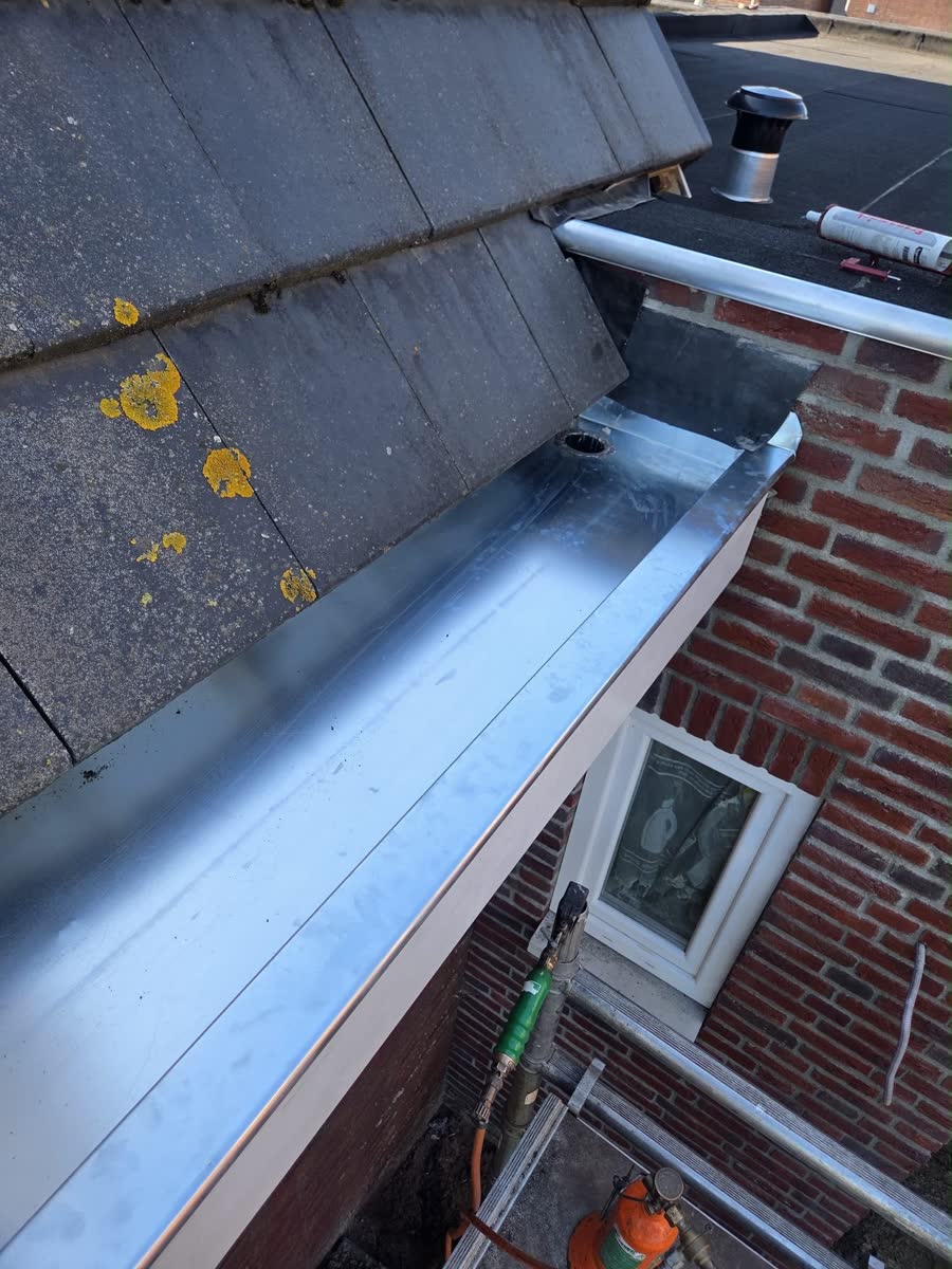 Nieuwe zinken dakgoot langs een hellend dak met bitumen shingles