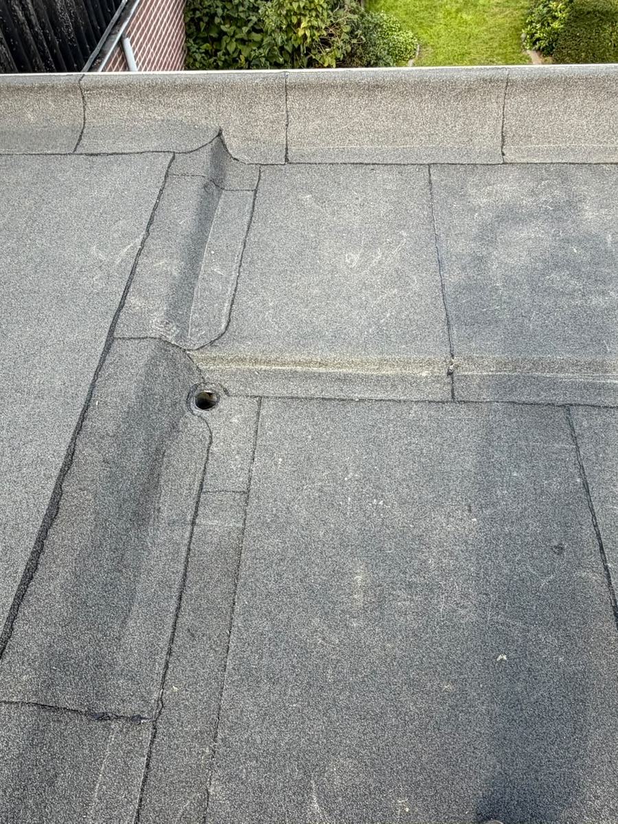 Dakrand van een plat dak met bitumen dakbedekking en een ronde doorvoer voor hemelwater